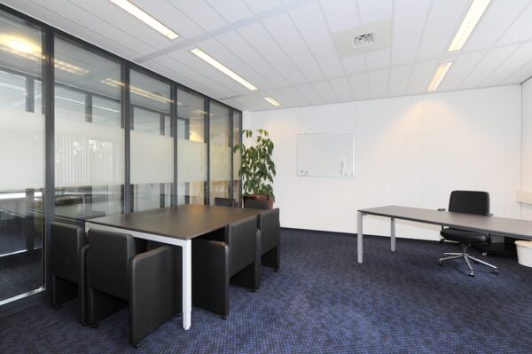Moderne kantoorruimte aan de Laan van S-Gravenmade met vergadertafel, bureau en glazen scheidingswand.